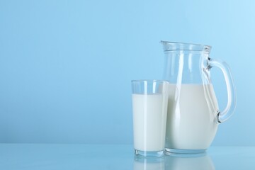 Jug and glass of fresh milk on light blue background, space for text
