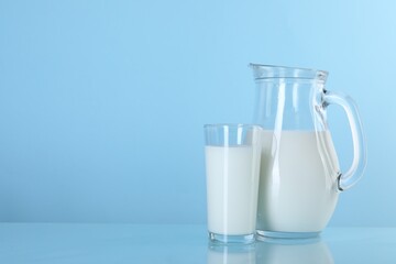 Jug and glass of fresh milk on light blue background, space for text