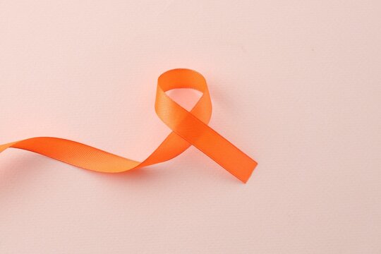 Orange awareness ribbon on beige background, top view