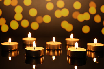Burning candles on mirror surface in darkness, bokeh effect
