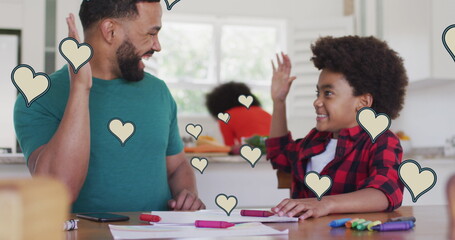 Image of social media heart icons over smiling biracial man and son doing homework - Powered by Adobe