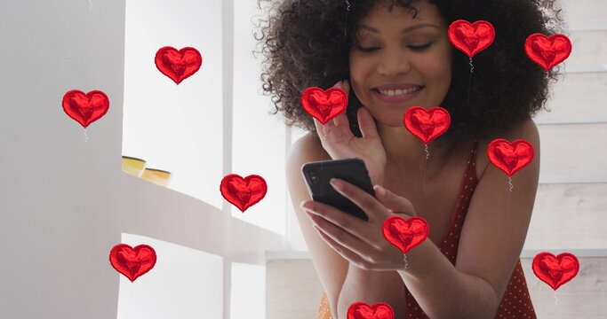 Image of numbers and social media heart icons over biracial woman using smartphone