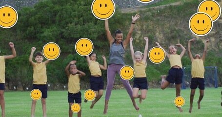 Image of emoji icons over diverse children with teacher jumping