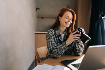 Cheerful young female photographer holding modern digital camera looking at screen choosing photos...