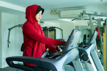 Athletic Asian Muslim Sports Woman Wearing Hijab and Sportswear Running on Treadmill. Energetic Fit...