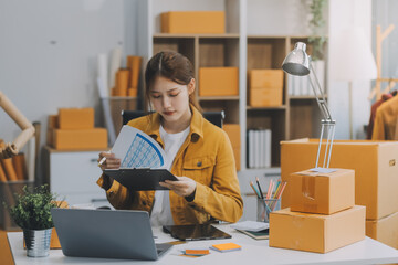 Asian SME business women use laptop computer checking customer order online shipping boxes at home....