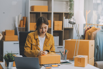 Asian SME business women use laptop computer checking customer order online shipping boxes at home....