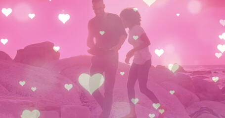 Image of heart icons over biracial couple at beach