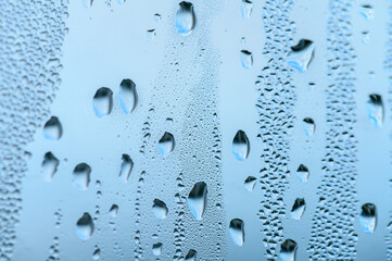 Blue background of natural water condensation, window glass with high air strong humidity, large drops drip