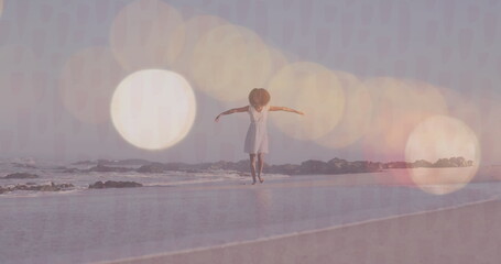 Image of lens flares over happy biracial young woman with arms outstretched walking at shore - Powered by Adobe