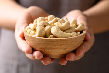 Raw cashew nuts in wooden bowl holding by hand, Food ingredient