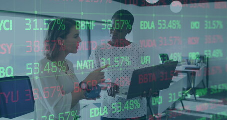 Image of trading board over diverse female coworkers standing and discussing reports on laptop