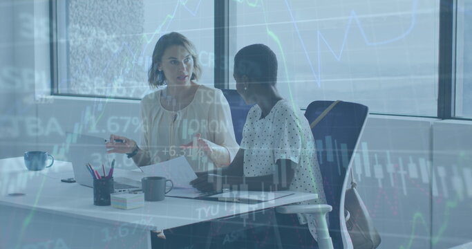 Image of graphs and trading board over diverse female coworkers discussing reports on laptop