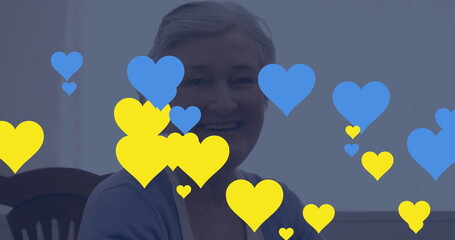 Image of blue and yellow hearts over senior caucasian woman using tablet