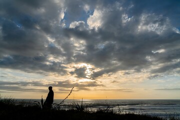 Silouette of man standing on a hill at sunset. Anawhata, Auckland, New Zealand.