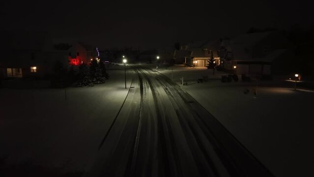 Snow covered upscale American neighborhood at night. Low flying aerial shot above dangerous road conditions after bizzard.