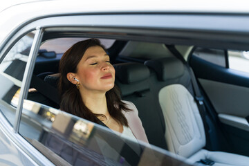 Confident businesswoman enjoys a peaceful moment in the backseat of a luxury car while being...