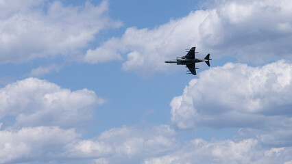 A military jet flies through a clear blue sky with minimal cloud cover.