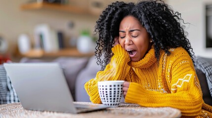 An African American woman yawning deeply as she works on a laptop from her cozy, modern home office