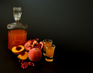 A bottle and two glasses of homemade fruit liqueur on a black background, next to pieces of a ripe...