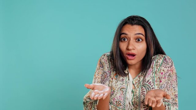 Indian woman shrugging shoulders, unable to provide answer, having detached apathy facial expression. Apathetic person doing hand gesturing showing lack of knowledge, studio background, camera B