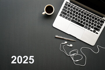 2025, text on black top with computer laptop, earphones and coffee. Top view.