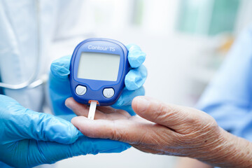 Asian doctor using digital glucose meter for check sample blood sugar level to treatment diabetes.