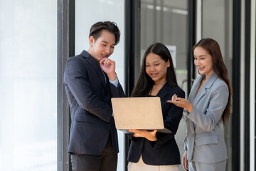 Smiling business team stand analyzing information on a laptop. Collaborative work and communication concept.