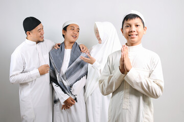 Asian muslim kid in skullcap showing greeting hands gesture with his family on the background