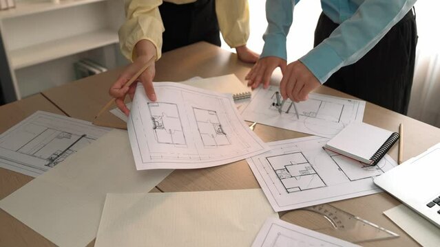 Architect and safety engineer discussion about building blueprint displaying on laptop on table with architectural document and wooden block scatter around at modern office. Closeup. Delineation.