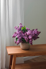 A bouquet of lilacs in a ceramic vase on a wooden oak table near window in the living room