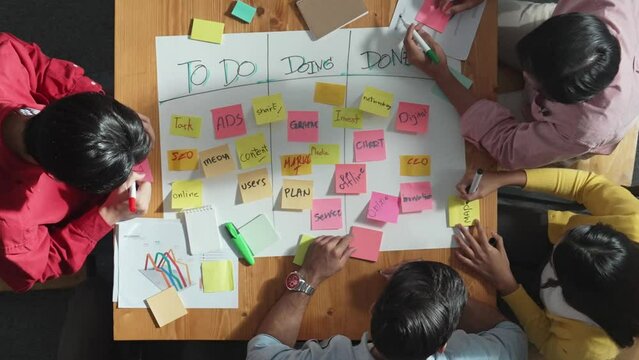 Top view of people writing and making scrum task board while writing marketing and planning strategy at colorful sticky notes. Smart team manage work performance by using kanaban board. Convocation.