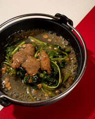sautéed kale served on a hotplate with pieces of meat and garlic