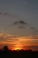 Natural Sunset Sunrise Over Field Or Meadow. Bright Dramatic Sky And Dark Ground. Countryside Landscape Under Scenic Colorful Sky At Sunset Dawn Sunrise. Sun Over Skyline, Horizon. Warm Colours.