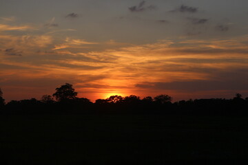 Natural Sunset Sunrise Over Field Or Meadow. Bright Dramatic Sky And Dark Ground. Countryside Landscape Under Scenic Colorful Sky At Sunset Dawn Sunrise. Sun Over Skyline, Horizon. Warm Colours.