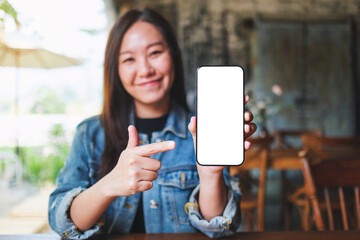 Mockup image of a young woman holding, showing and pointing finger at a mobile phone with blank...