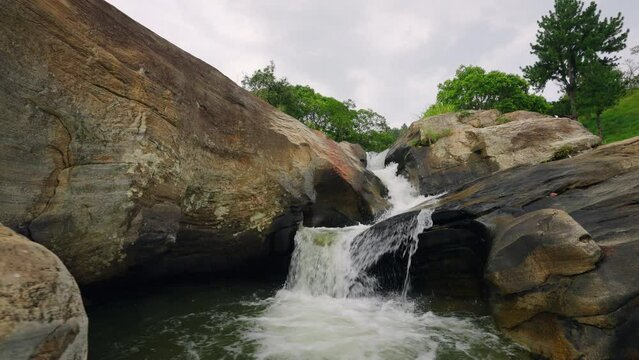 Low angle view of powerful waterfall cascading down rocky terrain, rich trees frame the scene. Nature scene with water flowing, ideal for travel, meditation, documentary backdrop. Slow motion.