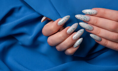 Female hands with blue nail design on blue textile background.