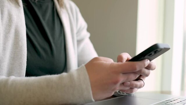 hands of a professional busily engaged with a smartphone in a well-lit office setting. The blurred laptop in the background and the minimalistic environment underscore a modern,