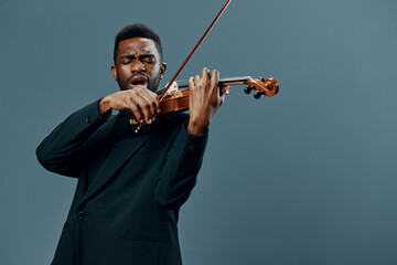 African American musician in a suit playing the violin on a gray background in a dramatic and elegant performance concept