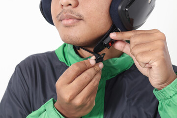 Close up portrait of Asian online taxi driver wearing green jacket and helmet demonstrating how to wear helmet correctly. Isolated image on white background