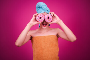A funny guy dressed as a drag queen and eating pink donuts. Pink background.