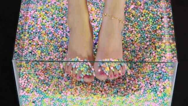 Pies con u&ntilde;as pintadas de rojor jugando con burbujas de colores.