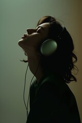 Silhouette of a woman with her eyes closed enjoying the music wearing headphones in soft and plain green background