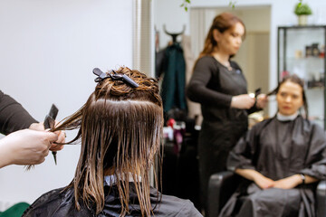 Woman professional hairdresser doing hair styling to client in beauty salon, applies balm to...