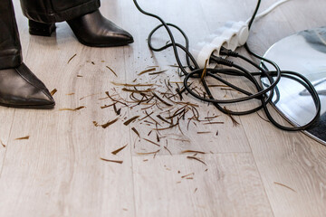 Cut hair on the floor in a beauty salon lies next to an extension cord for sockets.