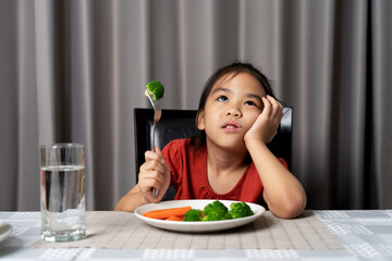 Little cute kid girl refusing to eat healthy vegetables. Children do not like to eat vegetables.