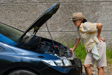 Side view: A woman is looking at the engine of her broken-down car