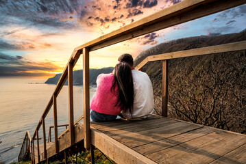married couple sitting together on the stairs and looking at sunset view