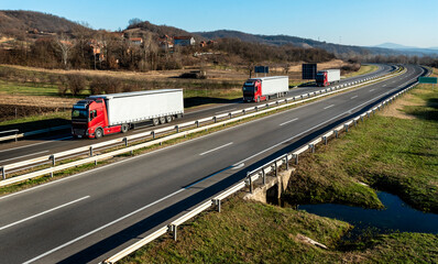 Convoy of three red trucks with white containers on highway, cargo transportation concept in...
